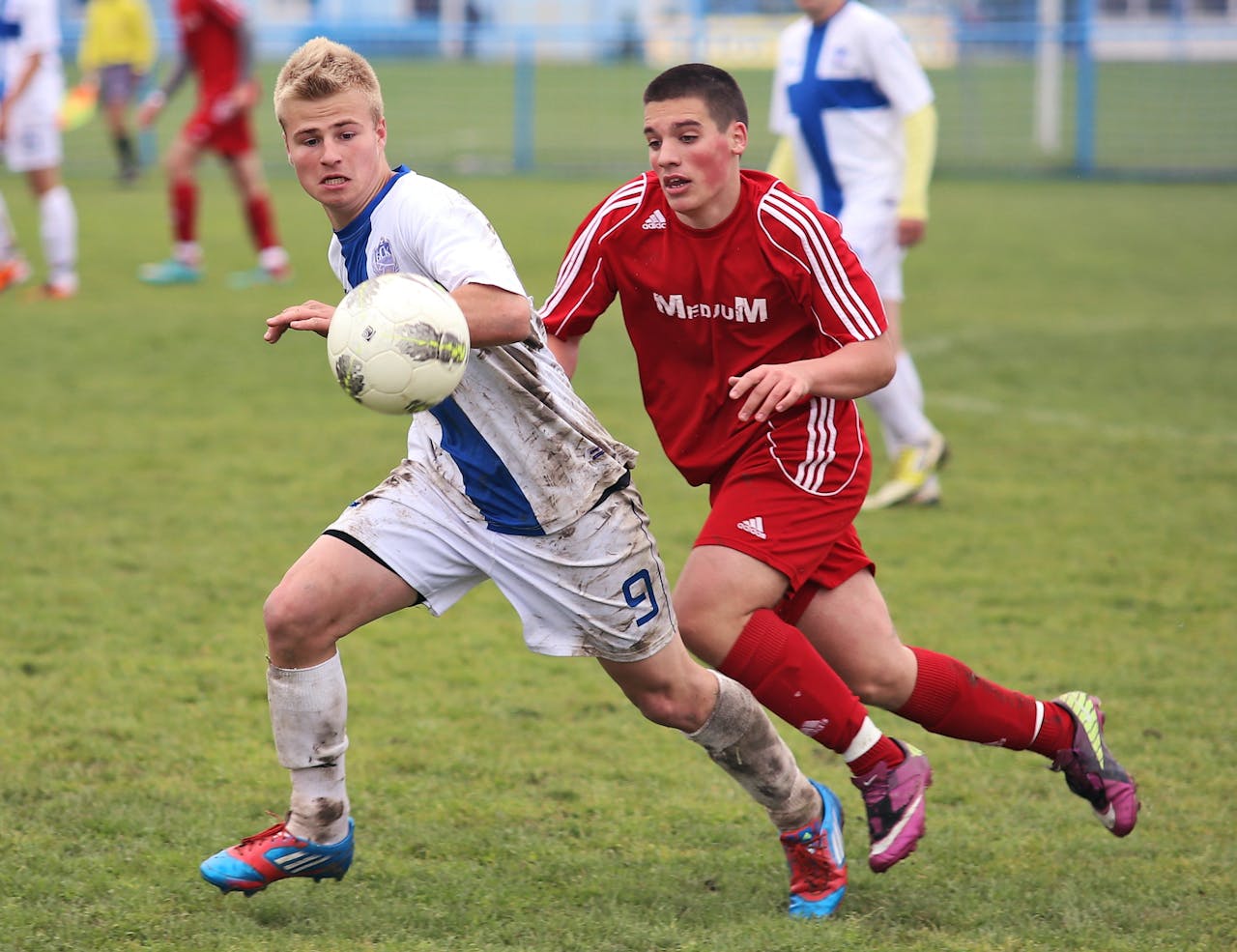 services-02 Two teenage soccer players competing fiercely on a muddy grass field.