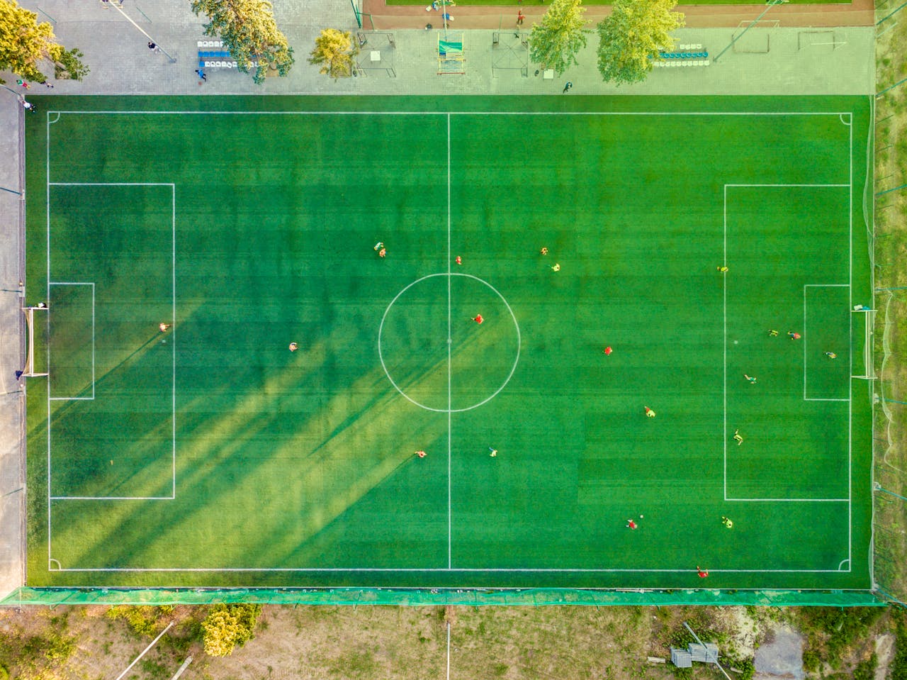 heros-img Aerial shot of a soccer game with players on a vibrant green field.