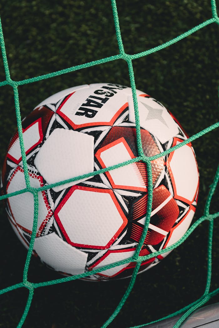 our-story Close-up of a soccer ball trapped in a net on a grassy pitch, perfect for sports themes.