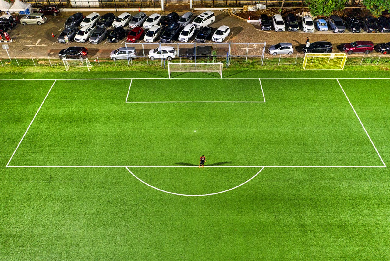 The Art of Drawing Readers In: Your attractive post title goes here Aerial view of a soccer field at night in Jakarta with a lone player casting a shadow under stadium lights.