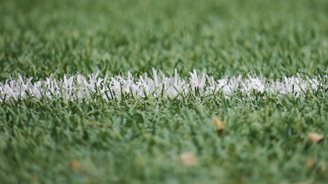 about-us Detailed close-up of a white line on artificial green turf, perfect for sports backgrounds.